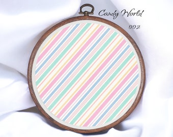 May include: A round wooden embroidery hoop with a white fabric background featuring a diagonal striped pattern in pink, blue, yellow, and green. The text "Candy World 002" is printed on the hoop.
