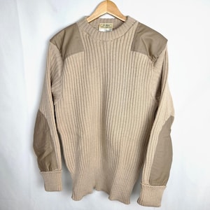 May include: A beige ribbed knit sweater featuring a crew neckline and long sleeves. The garment includes solid tan fabric patches on the shoulders and elbows. A label at the inner collar displays the text L.L. Bean Made in England.