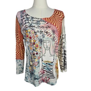 May include: A long-sleeve top featuring a graphic illustration of a person, abstract circular patterns in red, yellow, and black, and handwritten cursive text. The garment has a white base with red wavy lines on the sleeves and a scoop neckline.