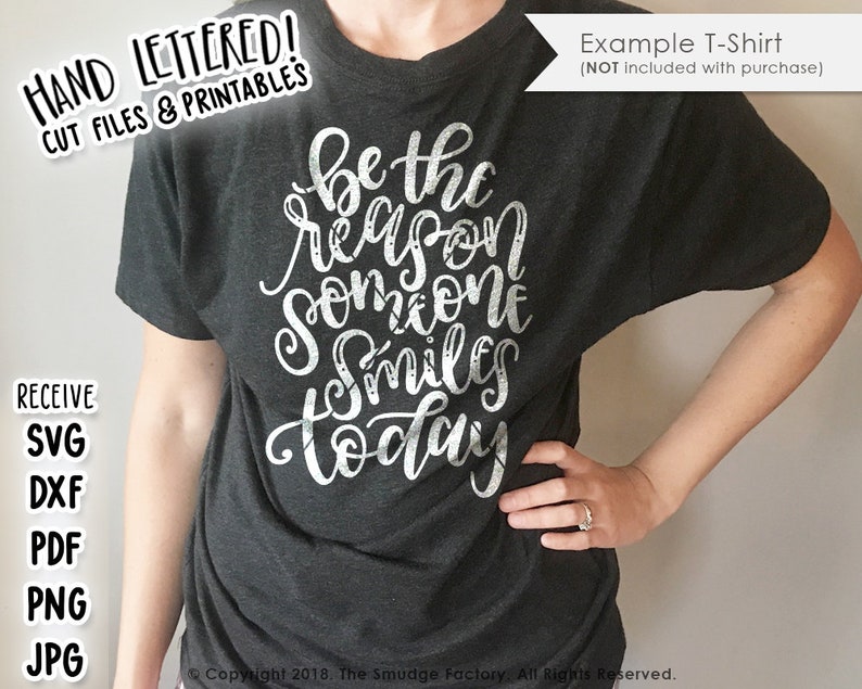 May include: A dark gray t-shirt with the text "be the reason someone smiles today" in white lettering. The text is in a handwritten style and has a distressed look.