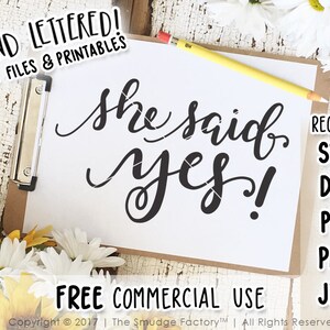 Può includere: Un biglietto bianco con calligrafia nera che recita "she said yes!" su uno sfondo marrone. Il biglietto è circondato da fiori bianchi e gialli. Il testo "RECEIVE SVG DXF PDF PNG JPG" è sul lato destro del biglietto.