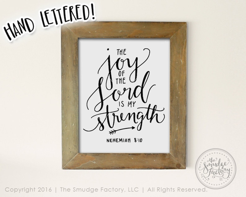 May include: A framed print with a white background and black calligraphy that reads "The joy of the Lord is my strength" with an arrow pointing to the right and the text "Nehemiah 8:10" below.