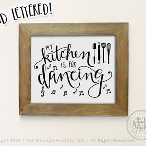May include: A framed print with the text "My kitchen is for dancing" in black cursive script. The text is surrounded by musical notes and kitchen utensils.