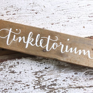 May include: A rustic wooden sign with the word "Tinkletoium" painted in white lettering.