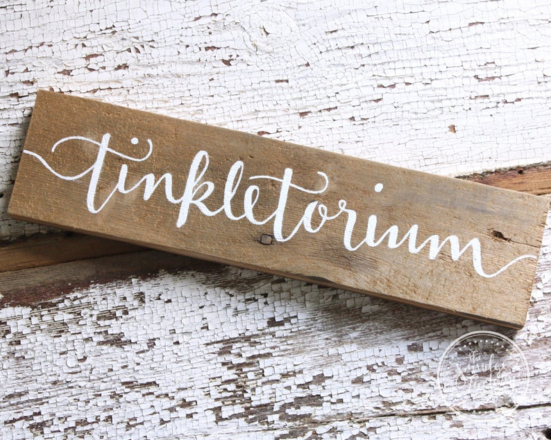 May include: A rustic wooden sign with the word "Tinkletoium" painted in white lettering.