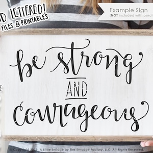 May include: A white wooden sign with black handwritten text that reads "be strong and courageous".