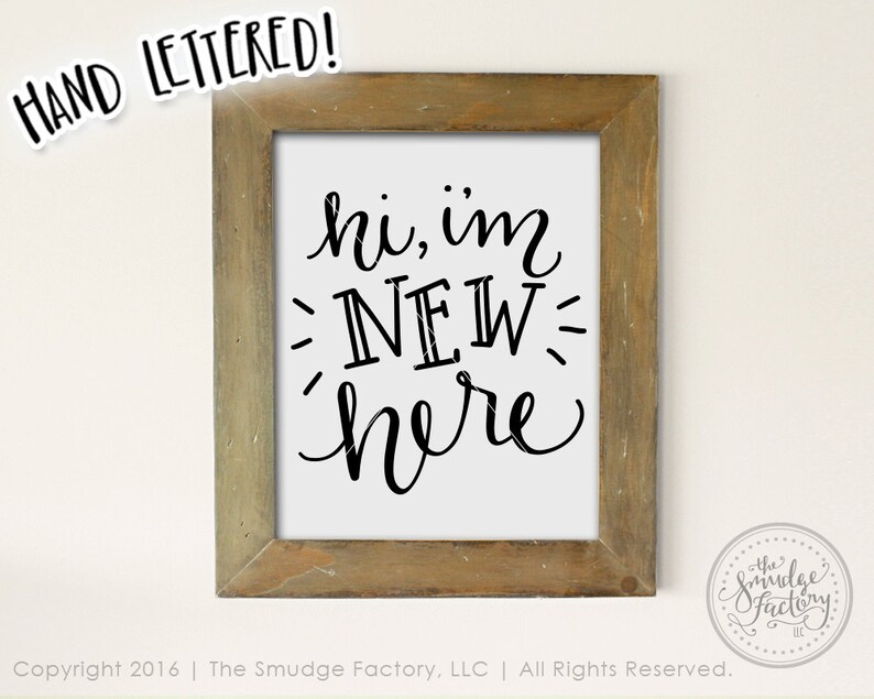 May include: A framed sign with the text "hi, im NEW here" written in black cursive font on a white background. The frame is made of wood with a light brown finish.