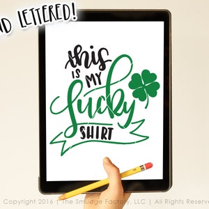 Peut inclure: Conception &agrave; la main sur fond blanc avec du texte noir et vert. Le texte dit "this is my lucky shirt" avec un tr&egrave;fle &agrave; quatre feuilles vert.