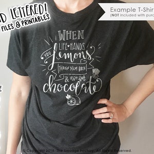 Puede incluir: Una camiseta gris con el texto "When life hands you lemons, throw them back & ask for chocolate" en letras blancas. El texto está rodeado por un gráfico de limón blanco y un gráfico de diamante blanco.