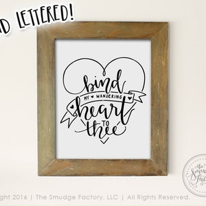 May include: A framed print with a black and white hand-lettered design that says "bind my wandering heart to thee" inside a heart shape.