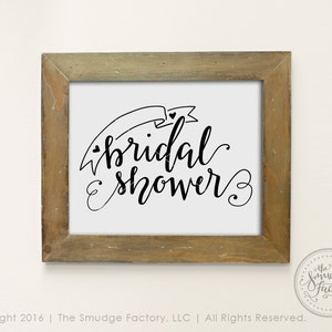 May include: A framed printable sign with the text "bridal shower" in black cursive script with a decorative banner and hearts.