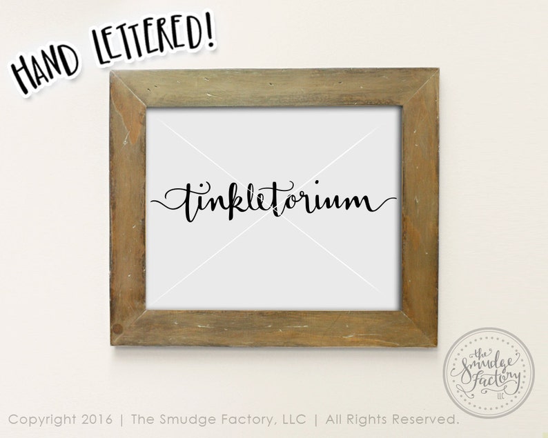May include: A framed print with the word "Tinkletorium" written in black cursive script. The frame is a light brown wood with a distressed finish. The print is on a white background.