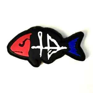 May include: A black fish-shaped patch featuring a red head section, a blue tail, and a white stylized graphic symbol in the center. The design has a bold outline and a flat, matte appearance, creating a distinct contrast between the colors.