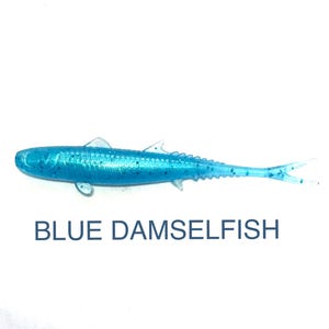 May include: A blue artificial fishing lure shaped like a fish, with fins and a forked tail. The lure has a textured body and is labeled "BLUE DAMSELFISH" in navy blue text.