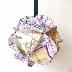 May include: A paper ornament shaped like a sphere, made from a map of Tulsa, Oklahoma. The ornament is decorated with various road names and highway numbers, including "Tulsa", "Gilcrease Mus", "Logan", "Slapout", and "Wann".