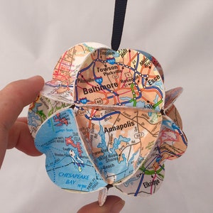 Może przedstawiać: Papierowa ozdoba w kształcie kuli, wykonana z mapy Baltimore w stanie Maryland i okolic. Ozdoba jest ozdobiona drogami, autostradami i punktami orientacyjnymi. Ozdoba jest zawieszona na czarnym sznurku.