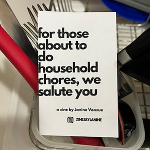 May include: A white card with black text that reads "for those about to do household chores, we salute you."  The card also includes the text "a zine by Janine Veazue" and a social media icon with the text "ZINESBYJANINE".