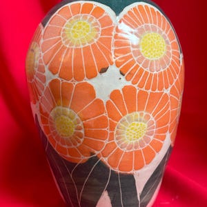 May include: A ceramic vase with a green top and a white body decorated with orange and yellow flowers. The vase has a rounded shape and a wide mouth.