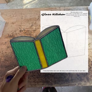 May include: A stained glass book with green pages and a yellow spine. The glass has a textured appearance. The words "Glass Kitchen" are visible, along with text stating the pattern cannot be sold or distributed.
