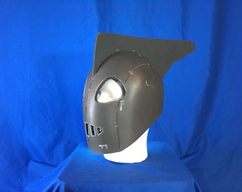 May include: A gray helmet with a fin on top. The helmet has a visor and a series of small holes on the front.