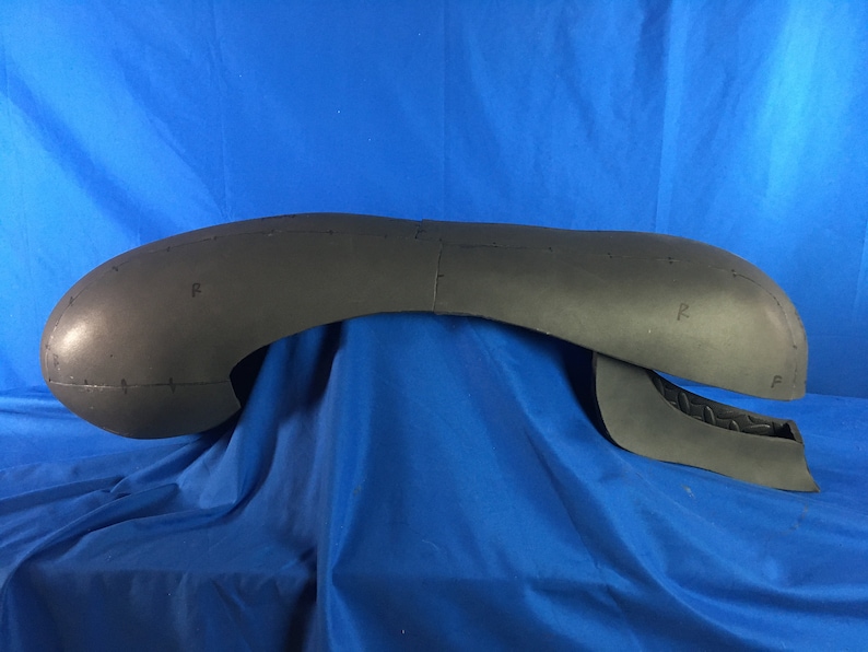 May include: A black foam alien head sculpture with markings and details. The head is in two pieces, with the top half resting on the bottom half.