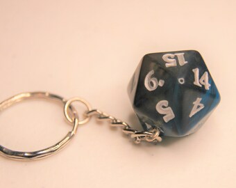 Op de afbeelding: Een blauwe en zwarte d20 dobbelsteen sleutelhanger met witte nummers. De sleutelhanger heeft een zilveren ring en ketting.
