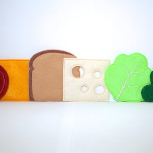 May include: Felt food pieces for pretend play, including a tomato, cheese, bread, lettuce, and pickles. The pieces are all different colours and shapes.