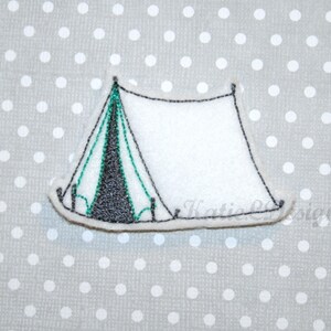 Peut inclure: Une applique en feutre blanc représentant une tente avec des coutures noires et vertes. La tente a un toit pointu et un rabat à l'avant.