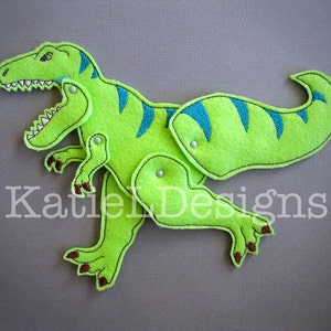 May include: A green felt dinosaur toy with blue accents. The dinosaur is made in sections that can be attached with snaps. The toy is designed for children to play with.