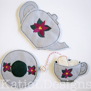 Può includere: Un set da tè in feltro grigio, con teiera, tazza e piattino. Ogni pezzo è decorato con un fiore di stella di Natale rosa e verde. La tazza contiene bustine di tè e un cubetto di zucchero. Per bambini.