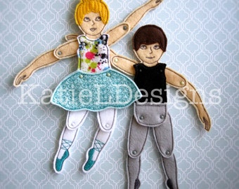 May include: Felt ballerina and ballet dancer dolls with articulated limbs. The ballerina wears a floral bodice and turquoise tutu, while the dancer is in a black top and gray pants. The dolls are connected with metal brads and are on a light blue patterned background. The text "Katie Designs" is visible.