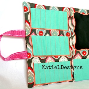 May include: A teal fabric organizer with three pockets and a chalkboard panel. The organizer has a pink handle and a paisley pattern with red, white, and gray accents. The text "KatieLDesigns" is printed on the bottom right corner.