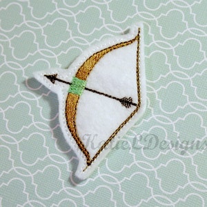 May include: A white felt patch with an embroidered gold bow and arrow. The arrow has a green fletching.