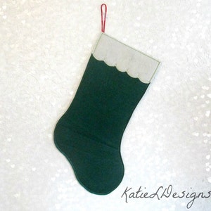 May include: A dark green Christmas stocking with a scalloped, light gray cuff and a red hanging loop. The stocking is made of felt and has the text "Katie L Designs" in the bottom right corner.
