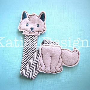 May include: A grey and white felt fox finger puppet with a black and white chevron pattern on the body. The fox has a brown nose and black eyes.