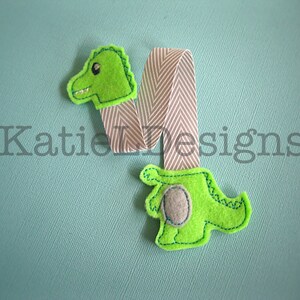 May include: Green felt dinosaur bookmark with a gray felt belly and a white and gray striped ribbon.