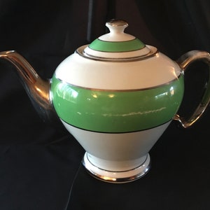 May include: A white teapot with a green and silver band design. The teapot has a silver spout and handle.