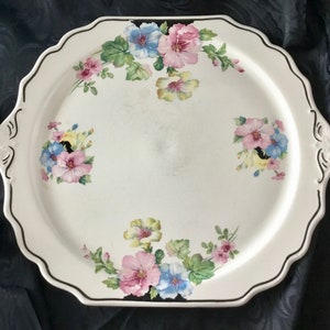 May include: White oval serving platter with a black rim and floral design. The flowers are pink, blue, yellow, and green.