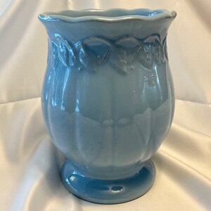 May include: A light blue ceramic vase with a scalloped rim and a pedestal base. The vase has a glossy finish and a decorative leaf pattern around the top. The vase is approximately 8 inches tall.