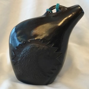 May include: Black ceramic pottery jug with a carved eagle design. The jug has a narrow neck and a wide base. It is decorated with a turquoise cord around the neck.