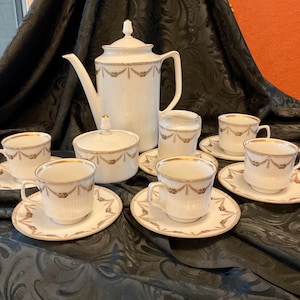 May include: A white porcelain tea set with gold trim. The set includes a teapot, creamer, sugar bowl, and four teacups and saucers.