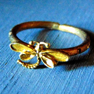 May include: A gold-toned ring featuring a dragonfly design. The dragonfly has a detailed body and wings.