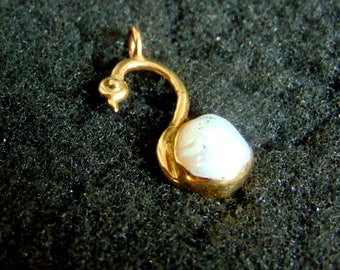 May include: A gold pendant featuring a stylized swan design with a white pearl at the bottom.