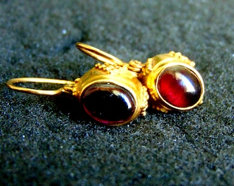 May include: A pair of gold earrings with red gemstone accents. The earrings have a simple, elegant design.