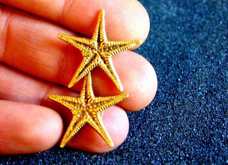 May include: Two gold-colored starfish ornaments. The starfish are stacked on top of each other.
