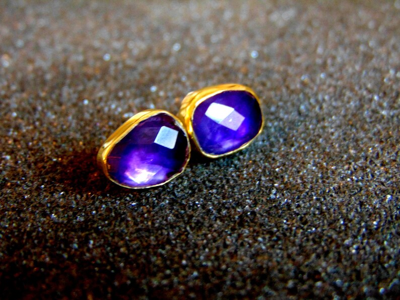Peut inclure: Une paire de boucles d'oreilles en or avec des accents de pierres pr&eacute;cieuses violettes. Les boucles d'oreilles sont de forme carr&eacute;e et ont une finition polie.