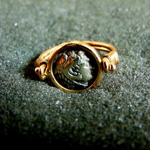 K&ouml;nnte beinhalten: Ein goldener Ring mit einer silbernen M&uuml;nze in der Mitte. Die M&uuml;nze zeigt das Profil eines Gesichts.