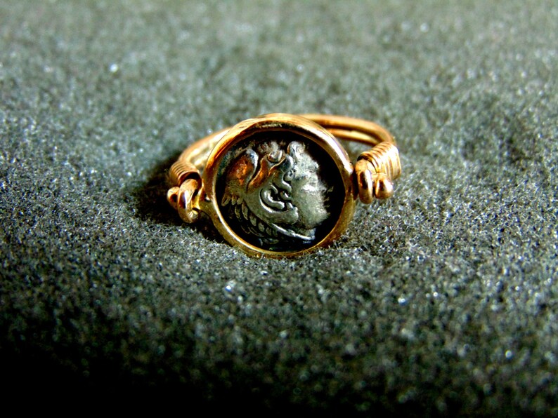 K&ouml;nnte beinhalten: Ein goldener Ring mit einer silbernen M&uuml;nze in der Mitte. Die M&uuml;nze zeigt das Profil eines Gesichts.