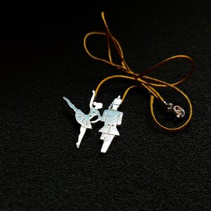 May include: A silver charm necklace with a pair of dancers, a man and a woman, on a gold cord.