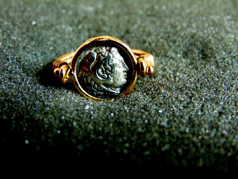 K&ouml;nnte beinhalten: Ein goldener Ring mit einer silbernen M&uuml;nze, die ein Profil eines menschlichen Kopfes zeigt. Die M&uuml;nze ist in einer Zargenfassung gefasst und der Ring ist verstellbar.